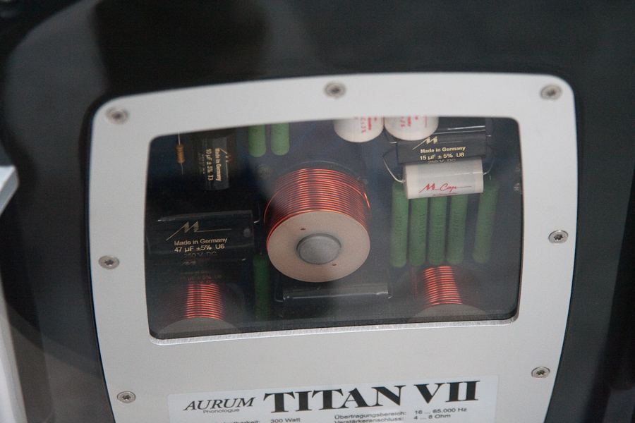 Passive crossover boards with inductor coils and capacitors visible through a window in the back of a Quadral Aurum Titan loudspeaker