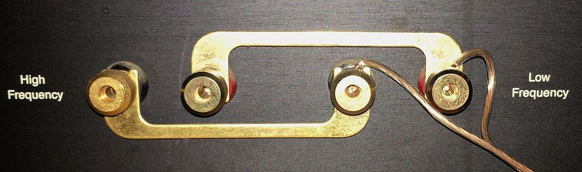 Bi-wire speaker terminals on the back of a JBL loudspeaker, joined by a brass jumper strap