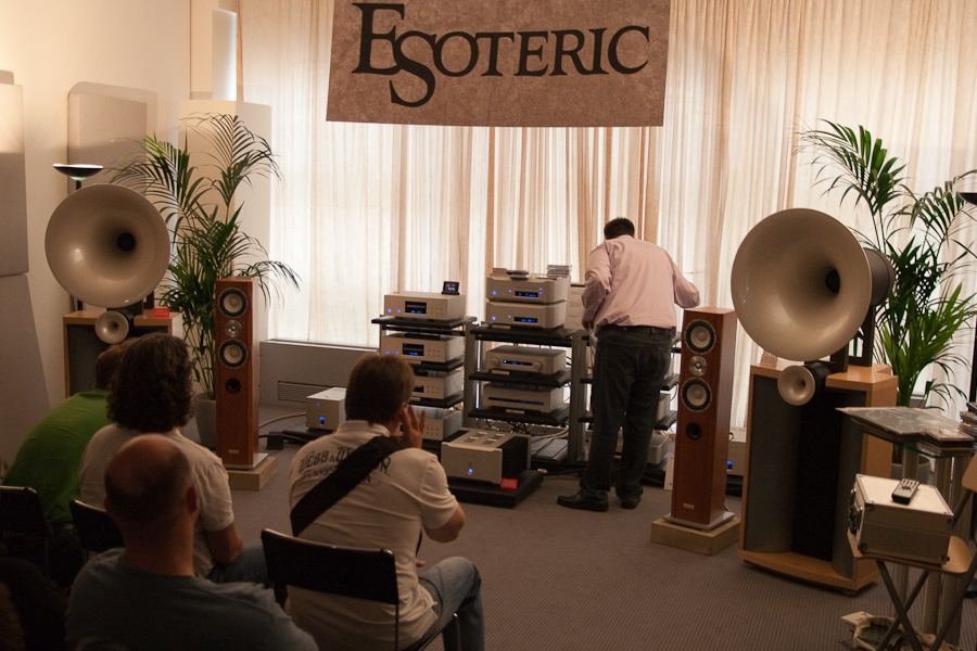 Trade-show listening room with a pair of large horn loudspeakers and a rack of electronics